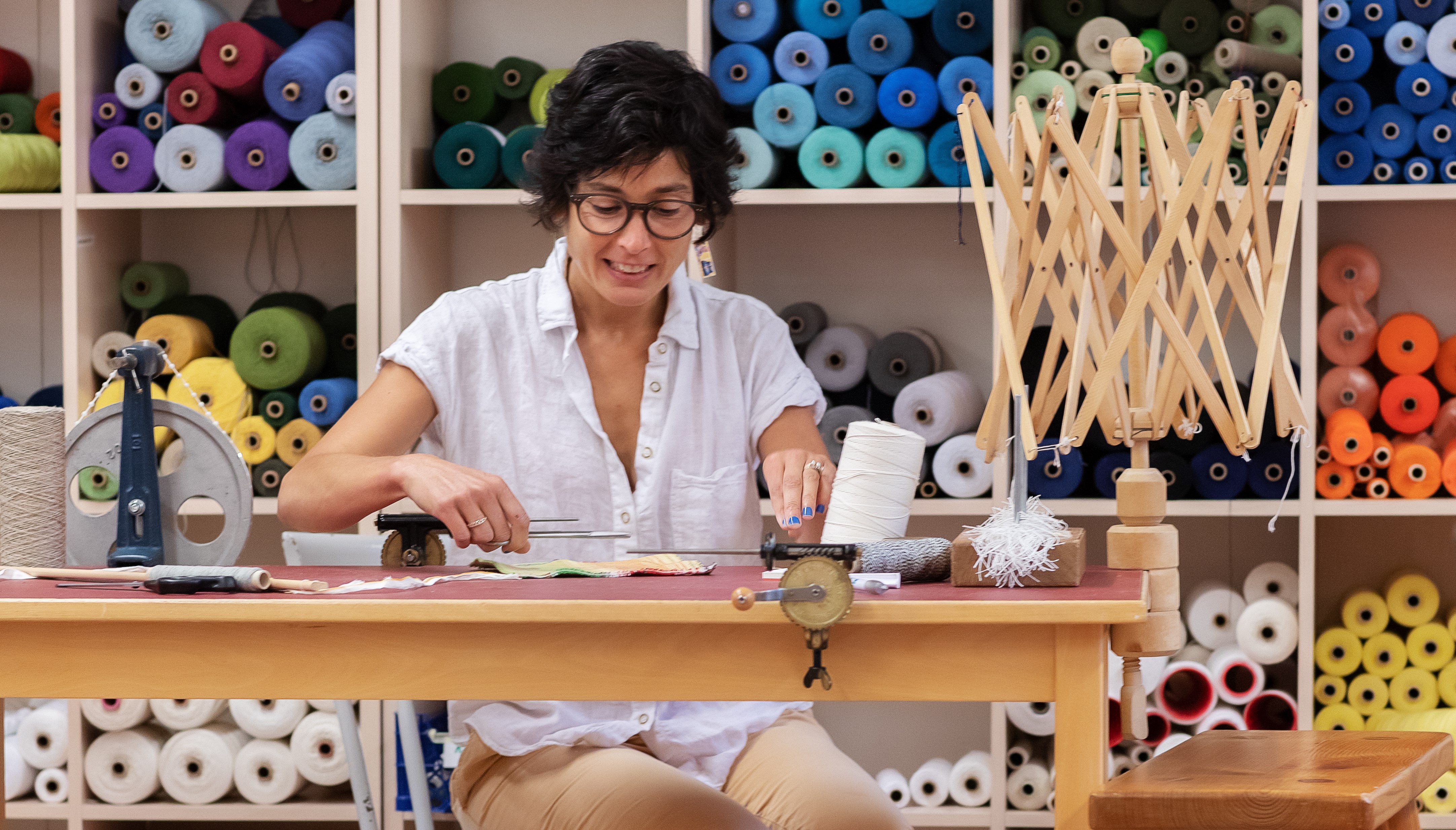 En deltagare som planerar sin väv vid ett bord. I bakgrunden syns trådar och garner i olika färger.